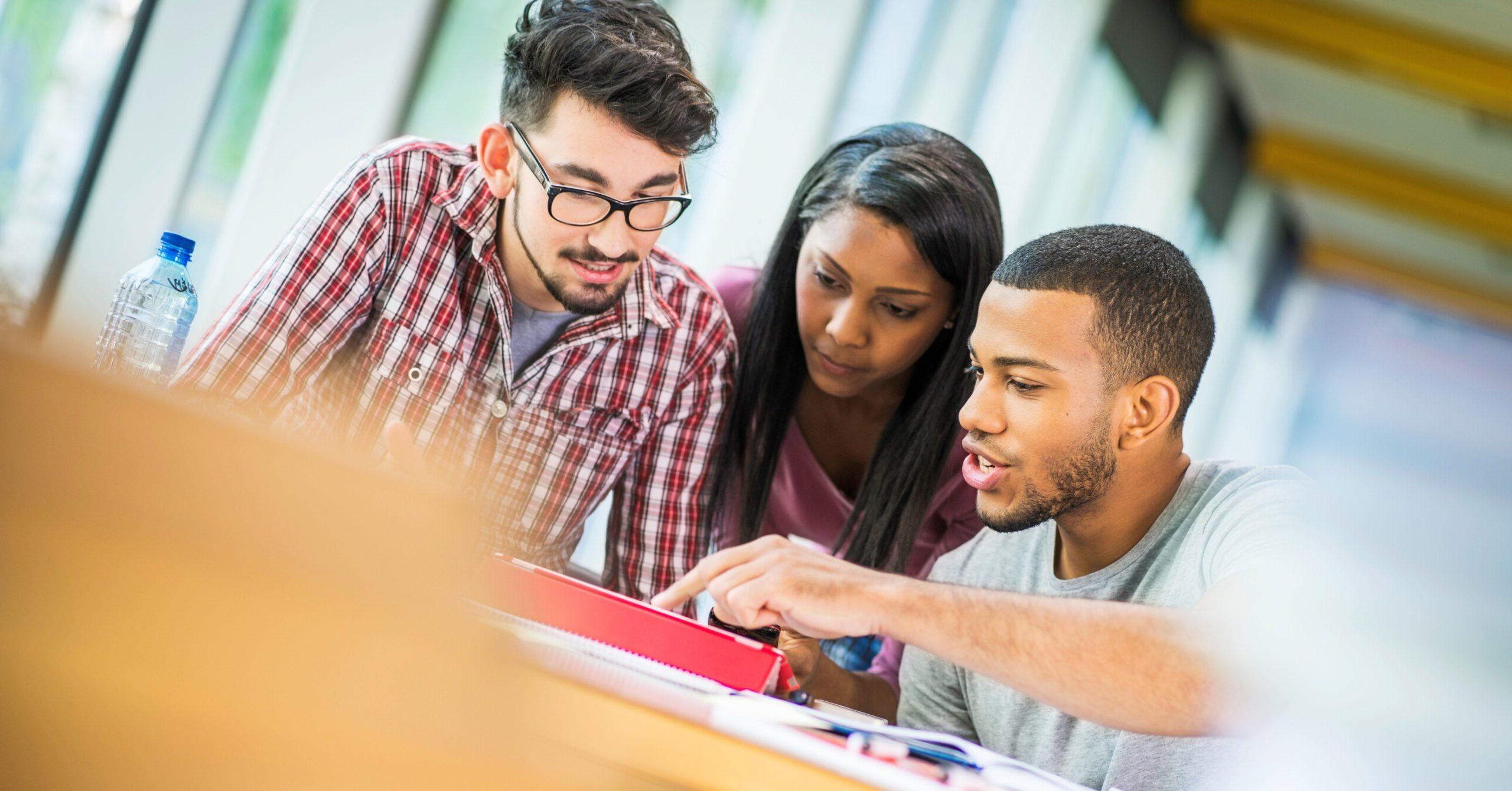 A group of students sit at a table and look at a laptop.